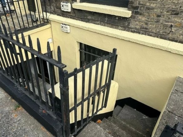 Basement entrance with black iron railing and yellow painted walls, XTRA security sign.