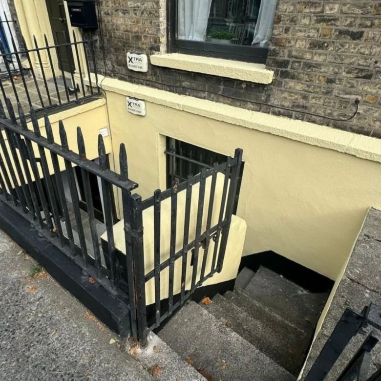 Basement entrance with black iron railing and yellow painted walls, XTRA security sign.