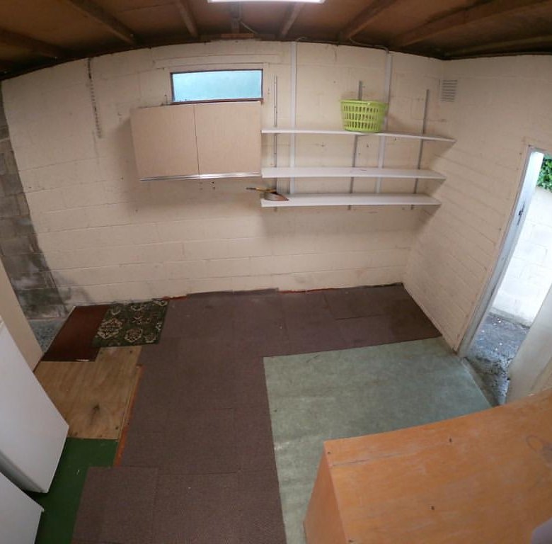 Basement storage room with shelves, refrigerator, and doorway to outside.