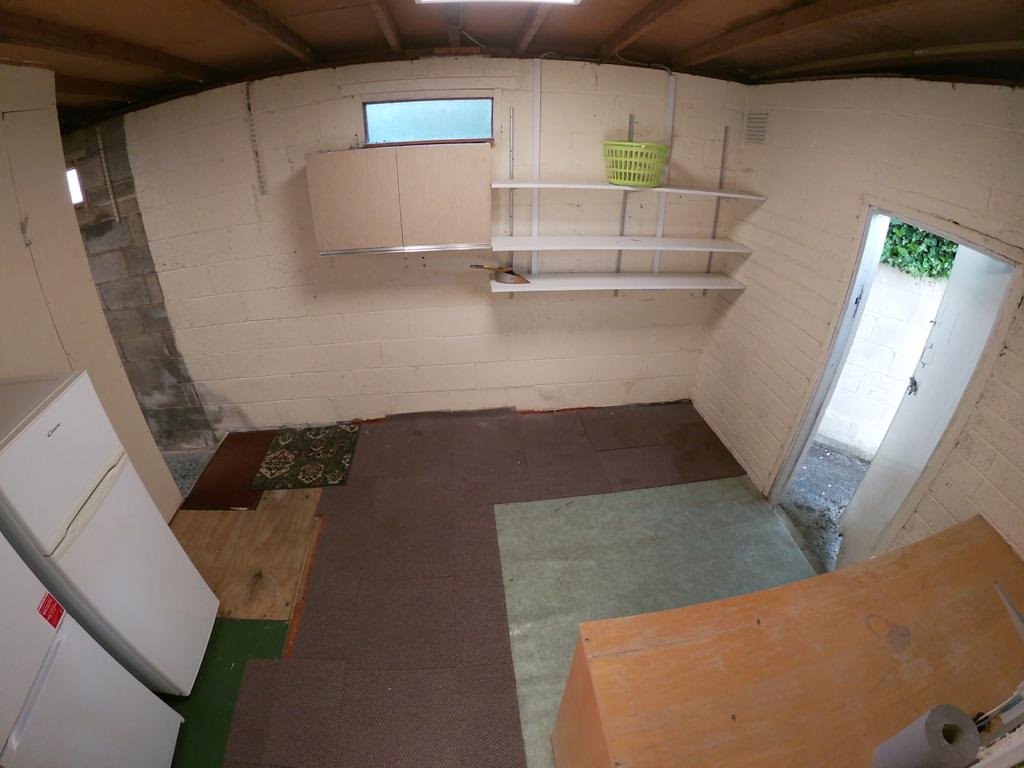 Basement storage room with shelves, refrigerator, and doorway to outside.