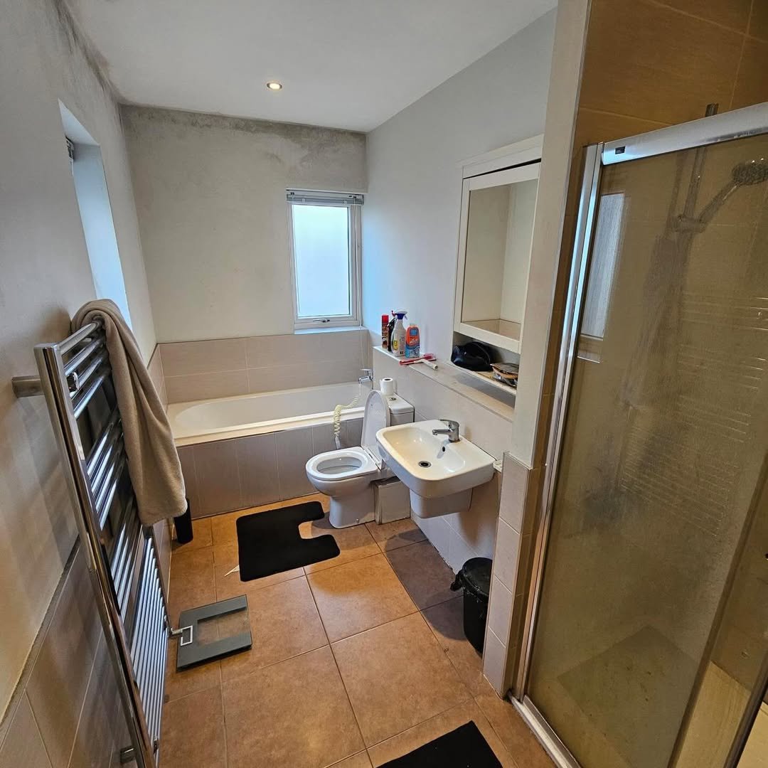 Bathroom with toilet, sink, tub, shower, towel warmer, and beige tile.