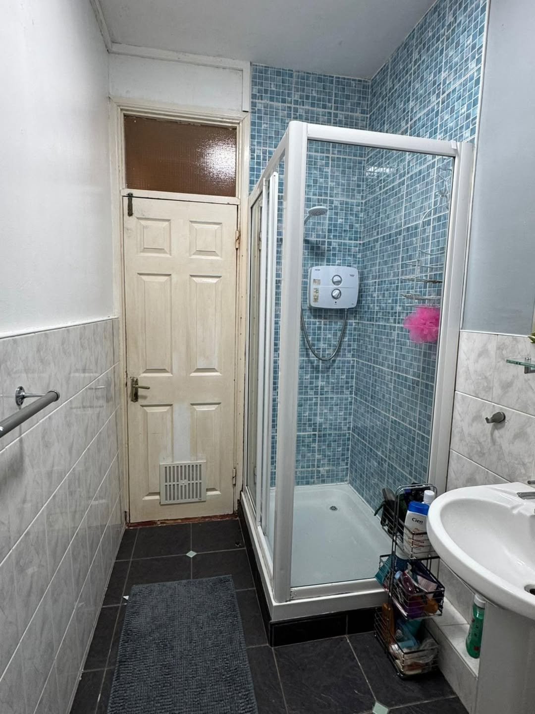 Bathroom with blue tiled shower, white sink, and aged door.
