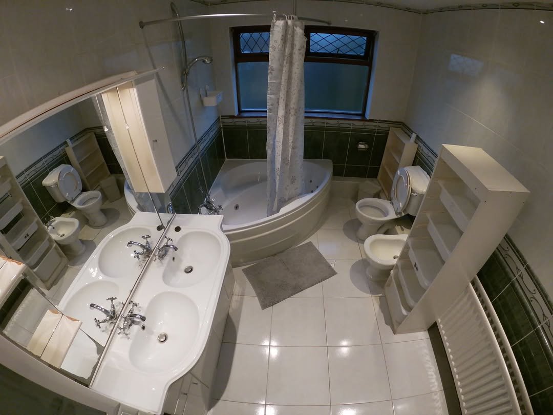 Bathroom with corner tub, double sink vanity, toilet, bidet, and white storage shelves.