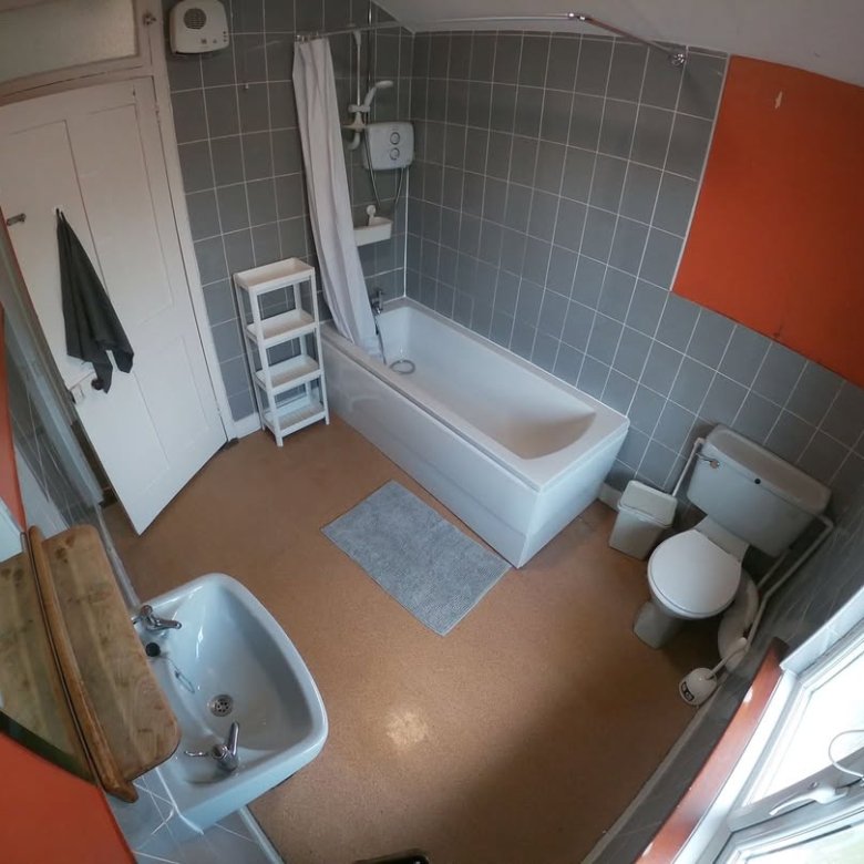 Bathroom with gray tile, white tub, toilet, sink, orange wall, and window. Small gray rug on brown floor.