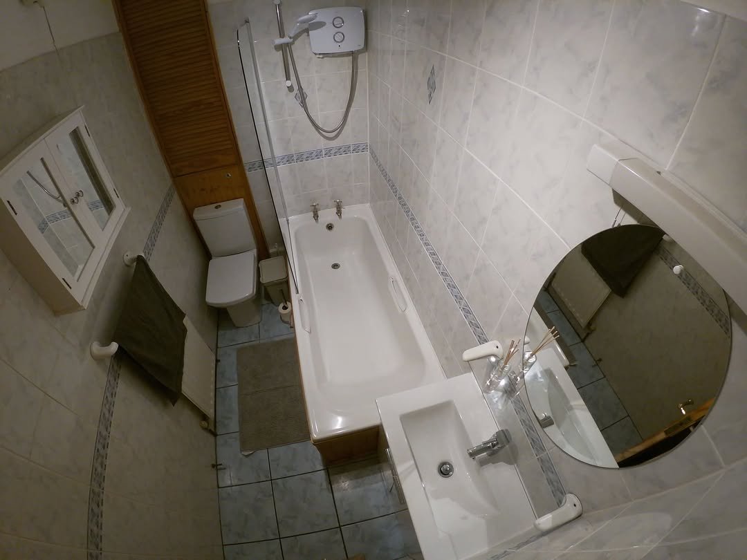 Bathroom interior with tub, toilet, sink, and cabinet. Tiled walls and floor.