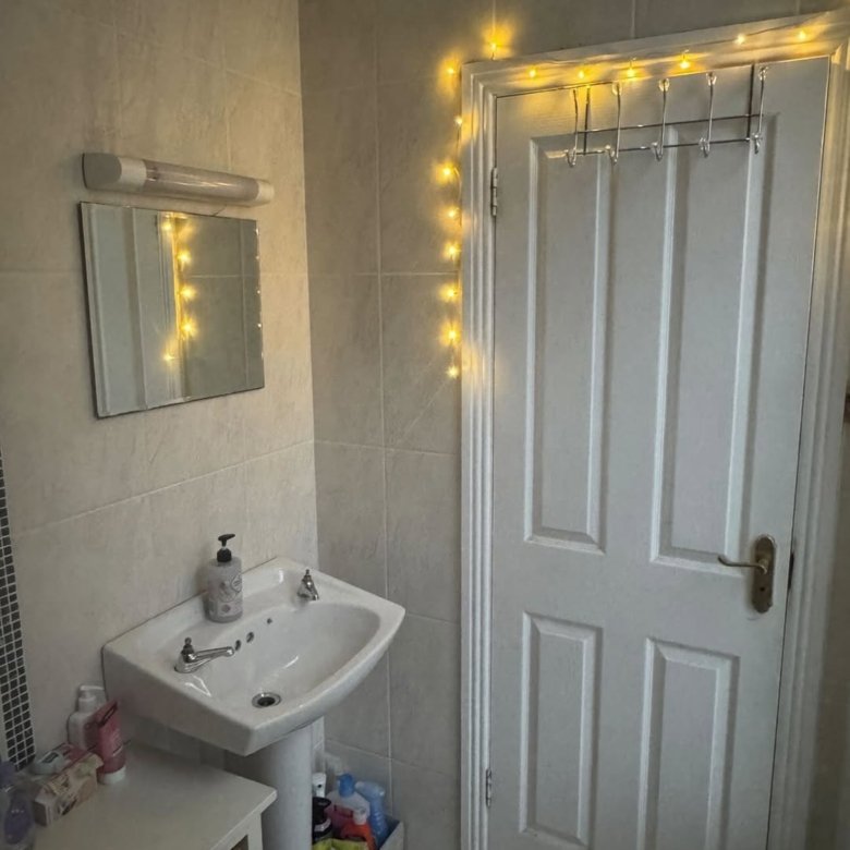 Bathroom with sink, mirror, fairy lights, and door with towel rack.