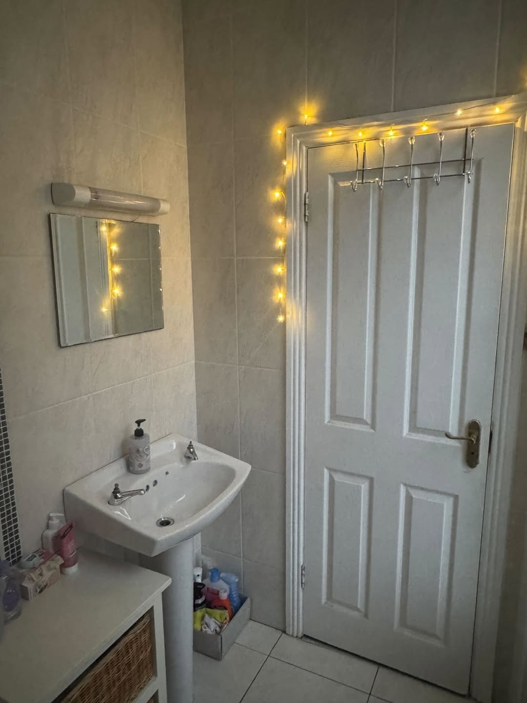 Bathroom with sink, mirror, fairy lights, and door with towel rack.