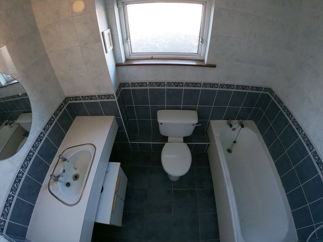 Bathroom with toilet, sink, and bathtub under a window. Blue and white tile design.