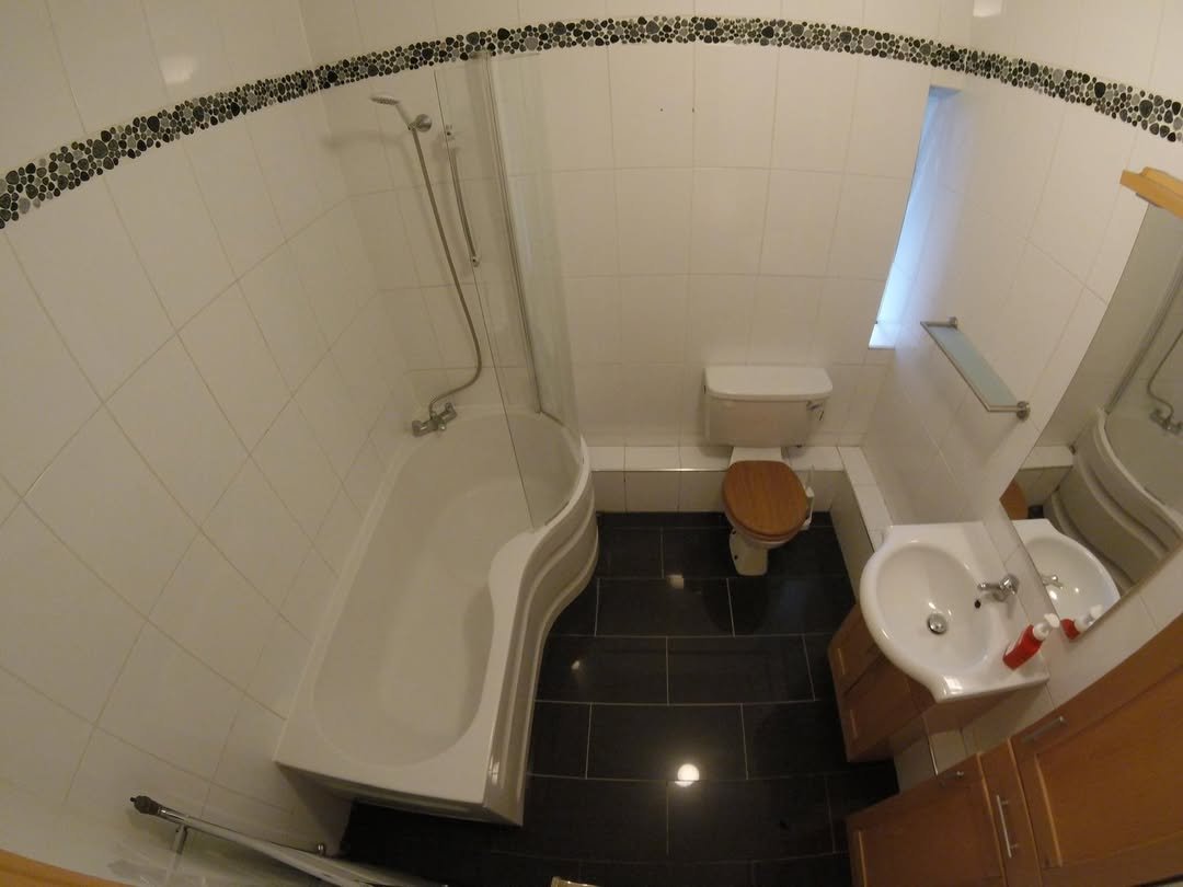 Bathroom with white tile, dark floor, bathtub, toilet, sink, and mosaic trim.
