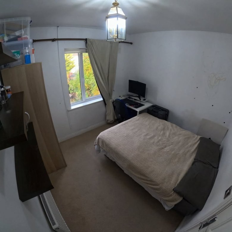 Cozy bedroom with bed, desk, computer, and window. Neutral color scheme.
