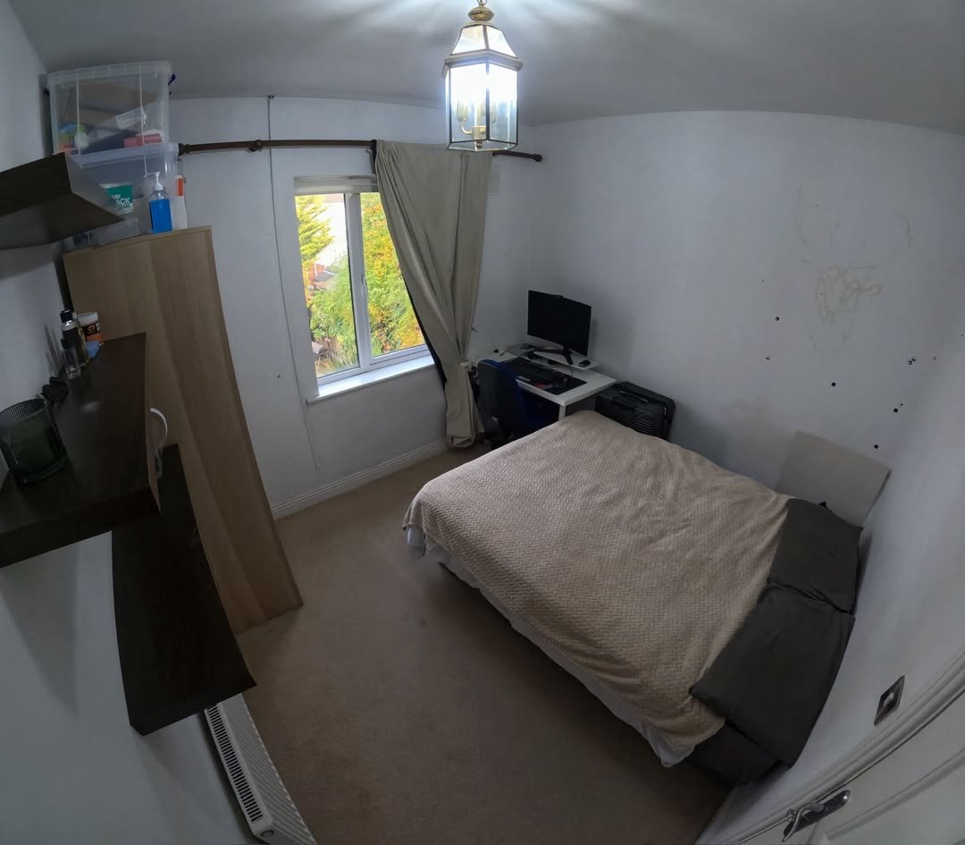 Cozy bedroom with bed, desk, computer, and window. Neutral color scheme.