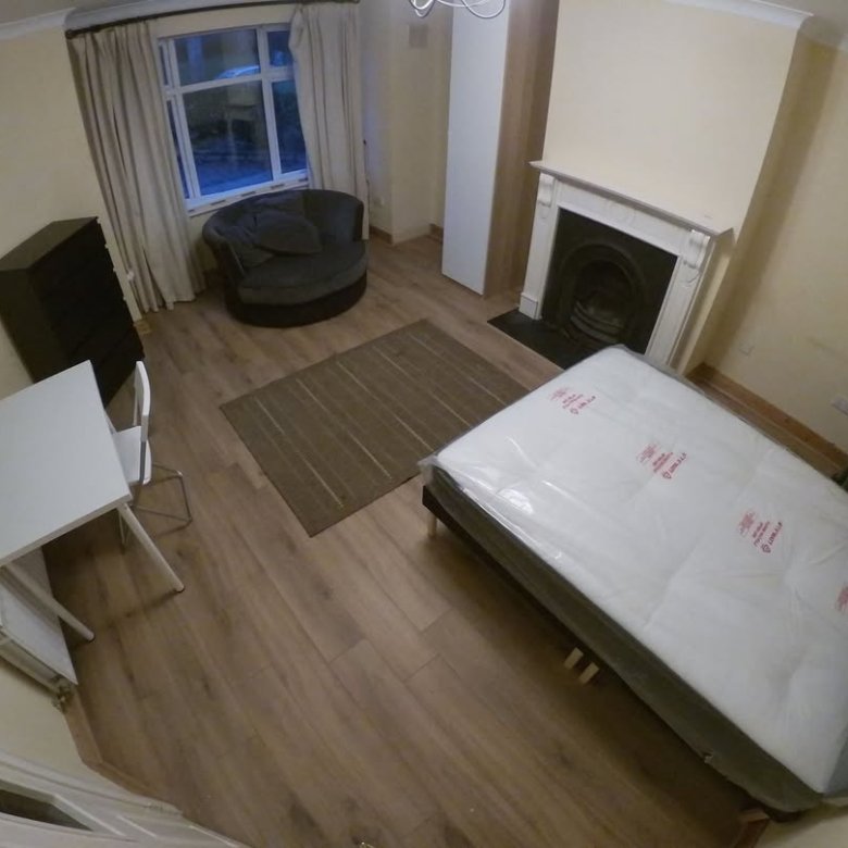 Bedroom with bed, desk, chair, fireplace, and round seat. Neutral colors.