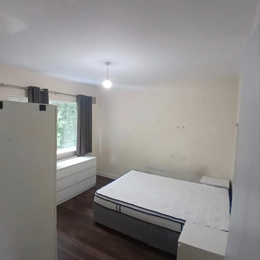 Bedroom with bed, dresser, wardrobe, and window with grey curtains.