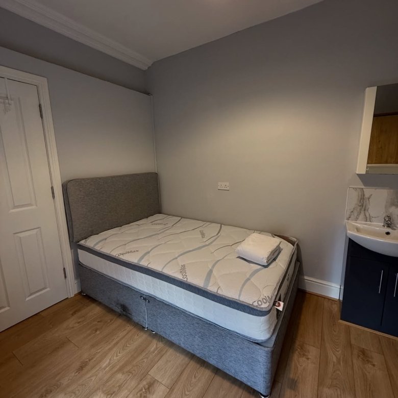 Cozy bedroom with bed, sink, and wooden floor. Neutral decor with warm lighting.