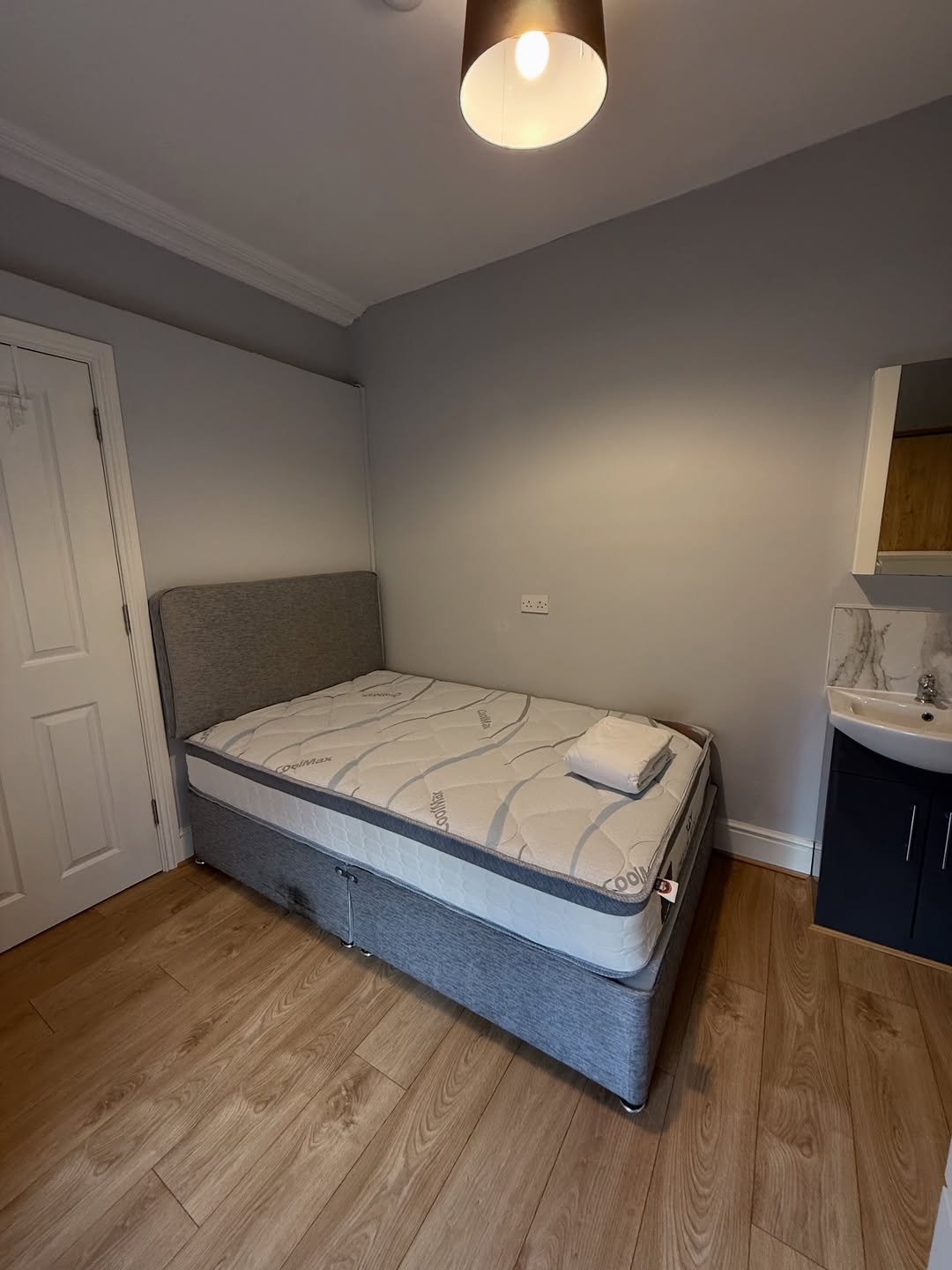 Cozy bedroom with bed, sink, and wooden floor. Neutral decor with warm lighting.