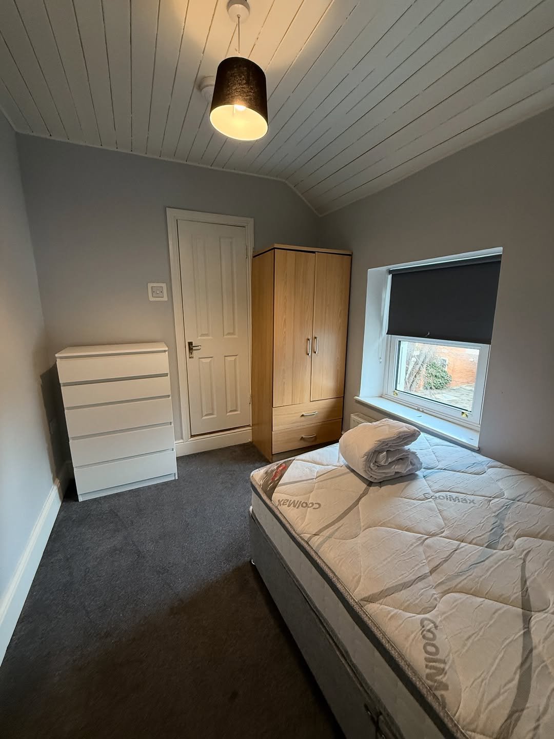 Bedroom with bed, wardrobe, chest of drawers, and window with blind.