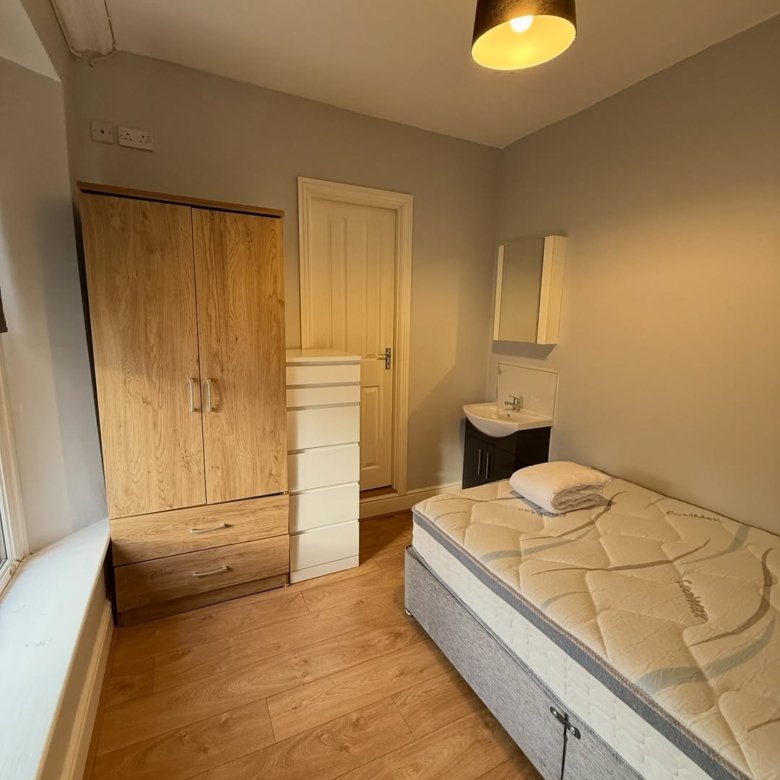 Bedroom with bed, wardrobe, drawers, sink, and wood floor.