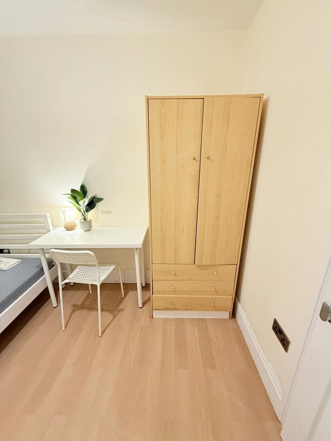 Bedroom corner with wardrobe, desk, chair, and bed. Light wood furniture, minimalist design.