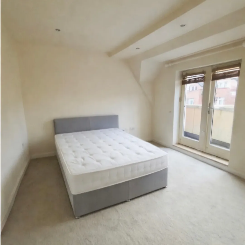 Bedroom with double bed, light carpet, and French doors leading to a balcony. Neutral decor.
