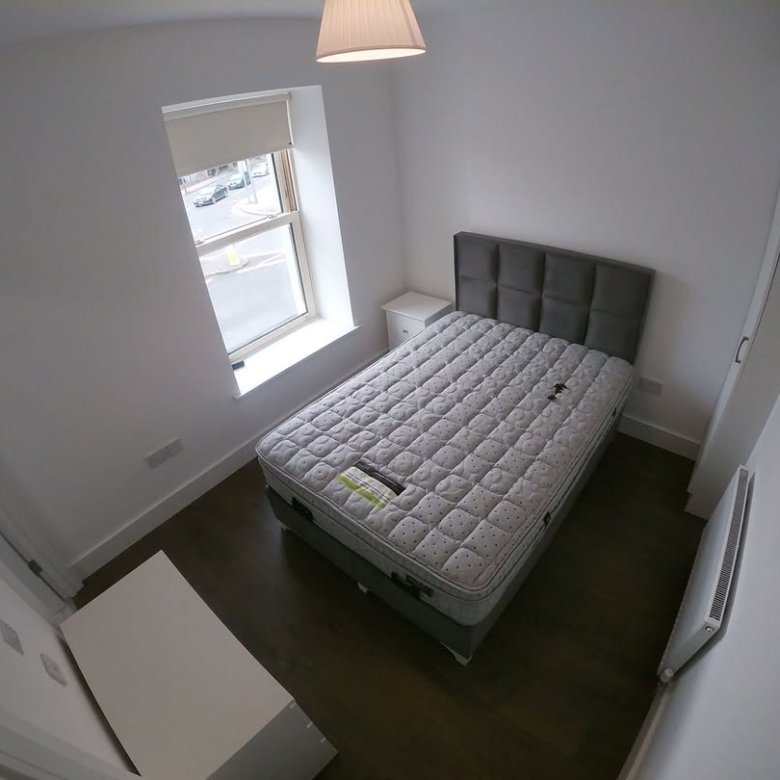Bedroom with double bed, white walls, and window with natural light. Minimalist interior design.