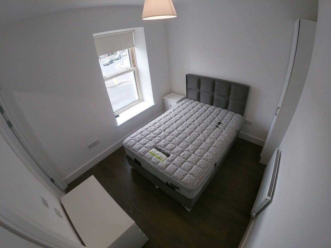 Bedroom with double bed, white walls, and window with natural light. Minimalist interior design.