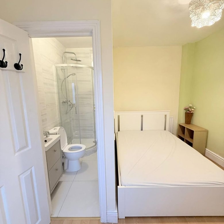 Bedroom with ensuite bathroom featuring shower, toilet, and sink. Single bed and small shelf unit visible.