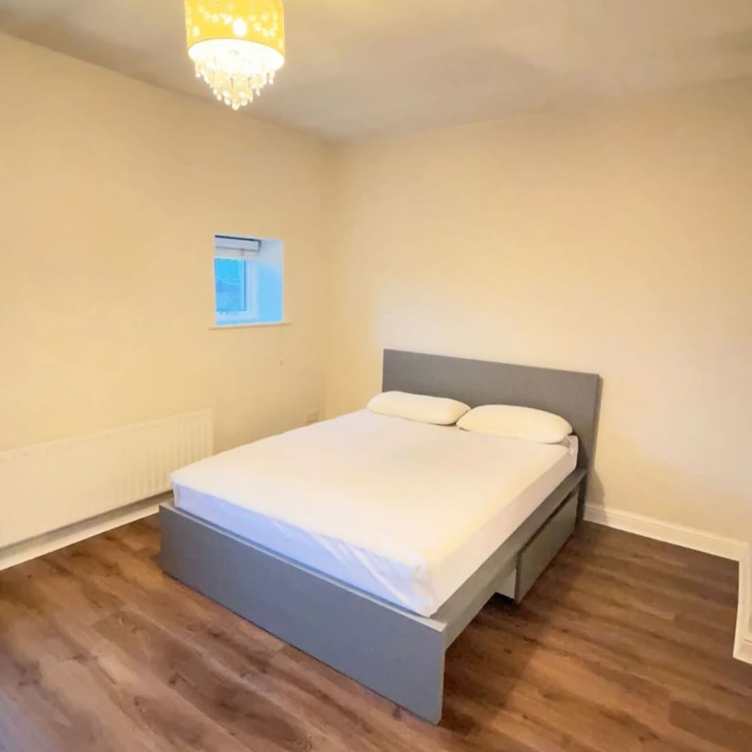 Bedroom with grey bed, white linens, and small window.
