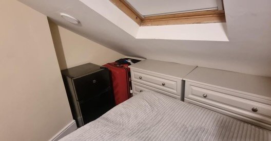 Bedroom with grey bedding, drawers, suitcase, and skylight in sloped ceiling.