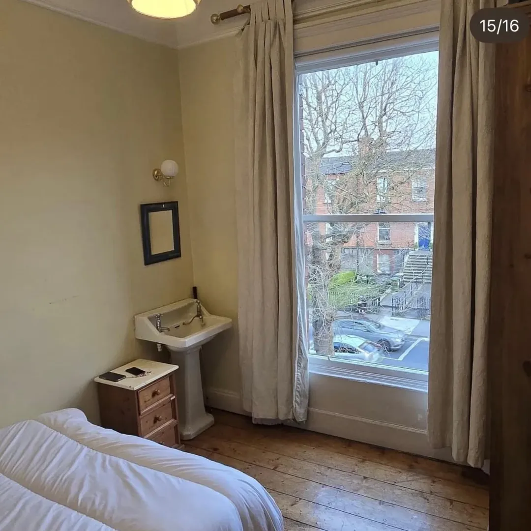 Bedroom interior with bed, sink, and window overlooking street.