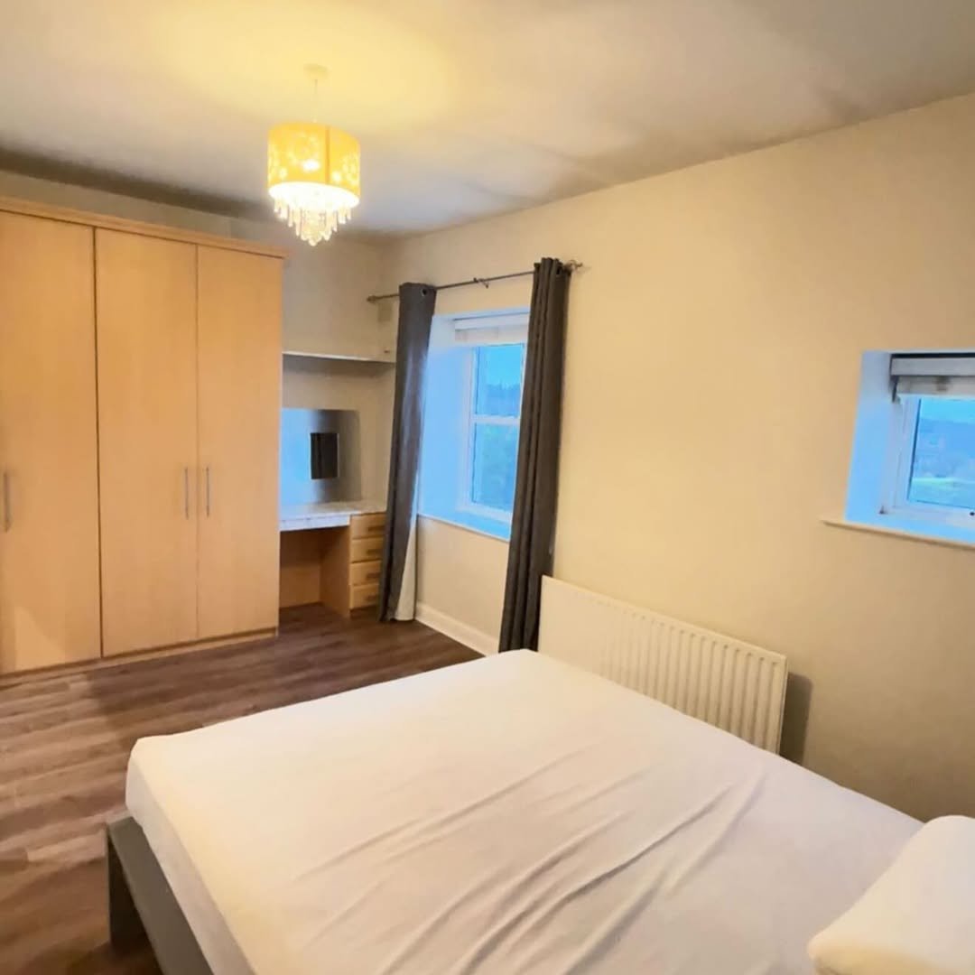 Bedroom interior with bed, wardrobe, desk, and windows. Neutral tones.