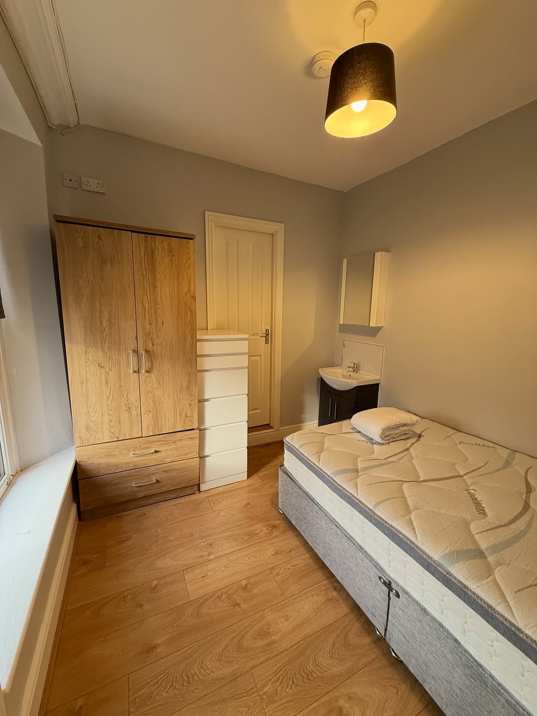 Bedroom interior with bed, wardrobe, chest of drawers, and sink area.