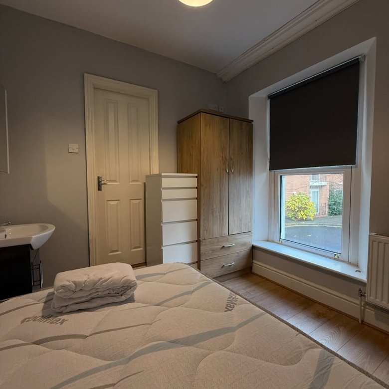 Cozy bedroom with bed, wardrobe, and sink near window.