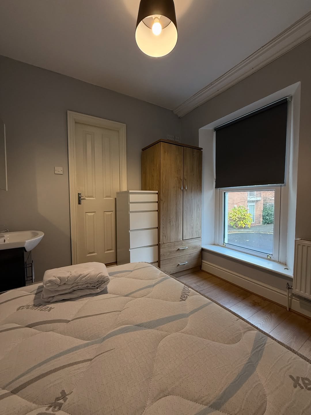 Cozy bedroom with bed, wardrobe, and sink near window.