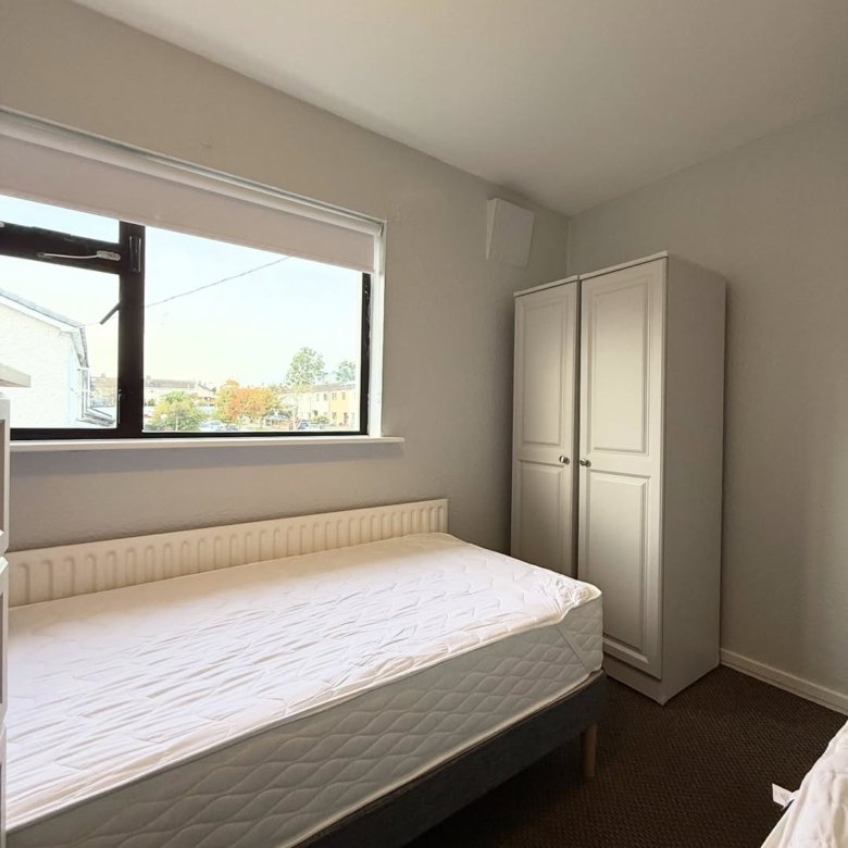 Bedroom interior with bed, wardrobe, and window. Neutral color scheme, carpeted floor.