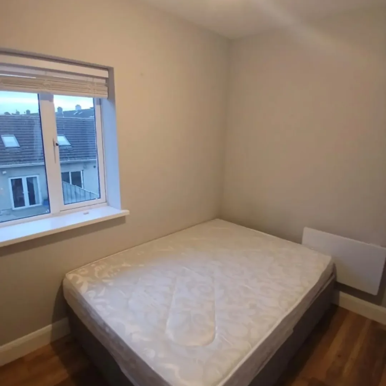 Bedroom interior with double bed, window, and hardwood floor.