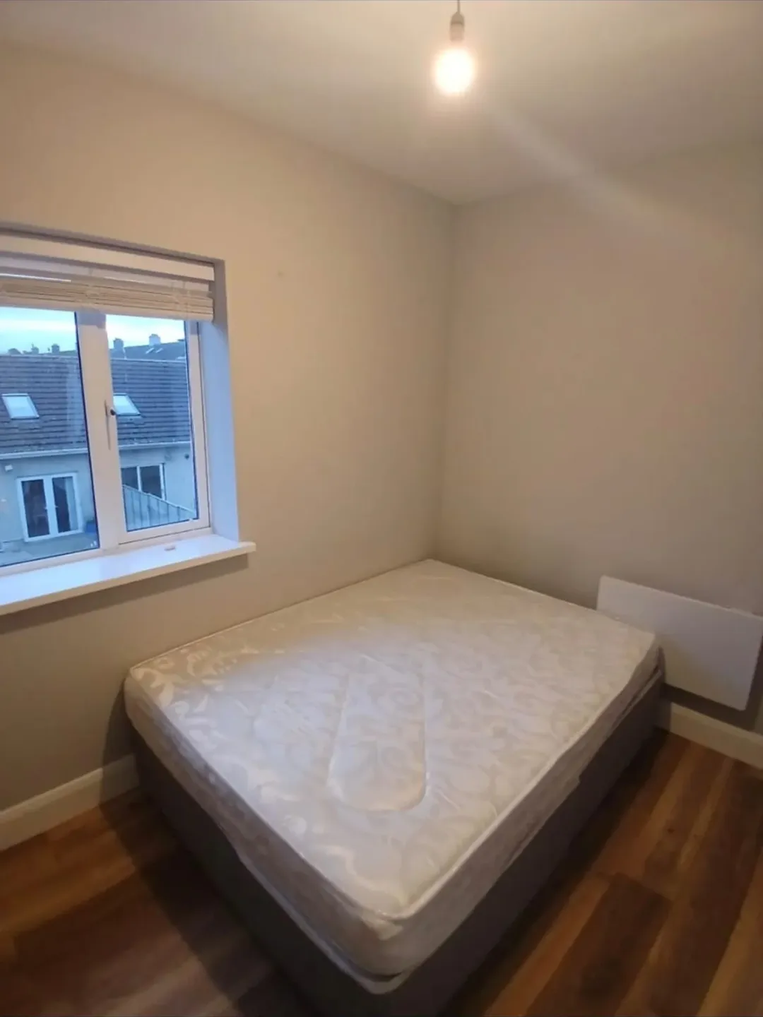 Bedroom interior with double bed, window, and hardwood floor.