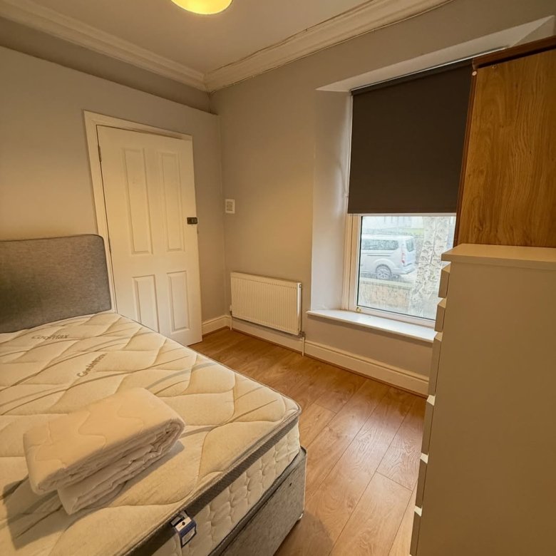 Cozy bedroom with made bed, radiator, and window with blinds.