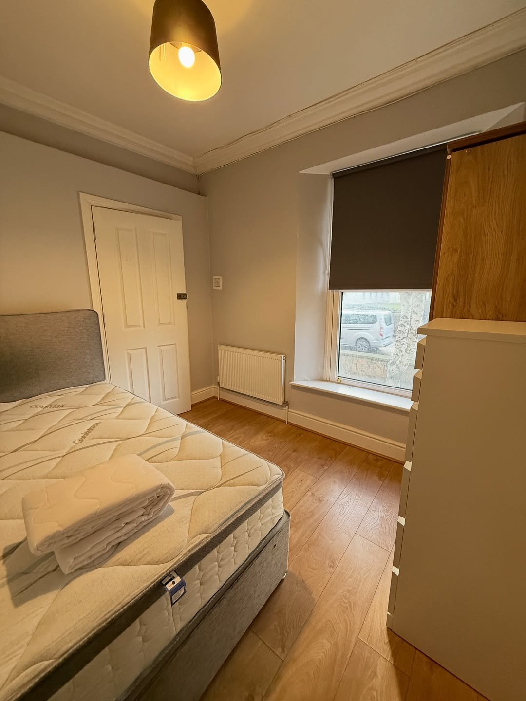 Cozy bedroom with made bed, radiator, and window with blinds.