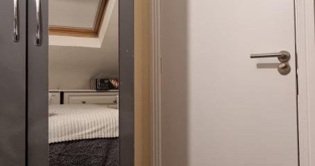 Bedroom interior reflected in wardrobe mirror, white door. Cozy room with sloped ceiling.