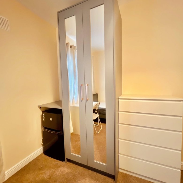 Bedroom with mirrored wardrobe, dresser, and mini fridge.