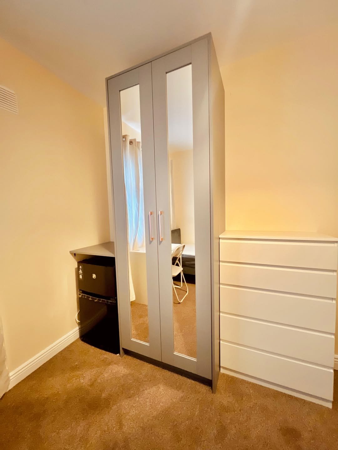 Bedroom with mirrored wardrobe, dresser, and mini fridge.