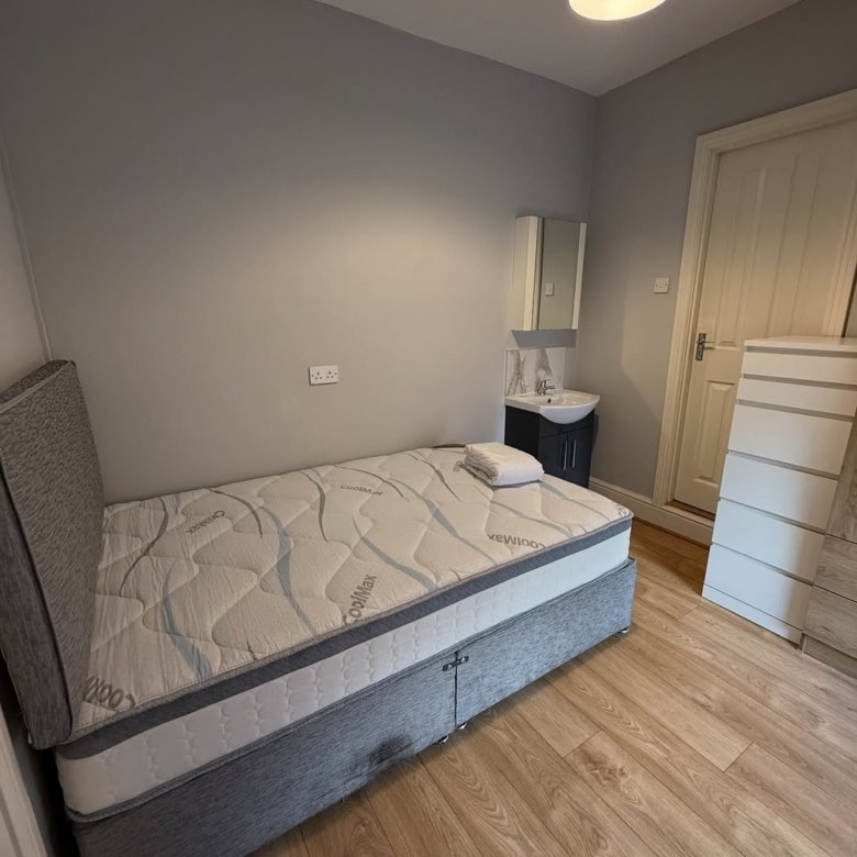 Cozy bedroom with single bed, sink, and dresser in neutral tones.