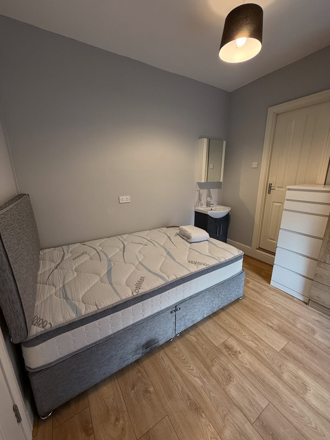 Cozy bedroom with single bed, sink, and dresser in neutral tones.