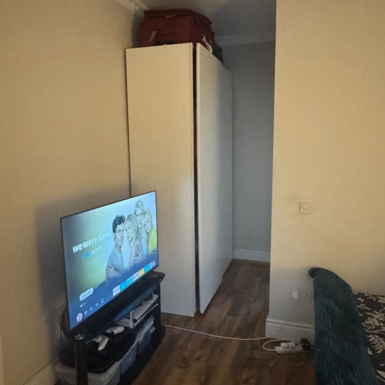 Bedroom interior with TV, wardrobe, and luggage on top. Text on screen: "We Were Liars".