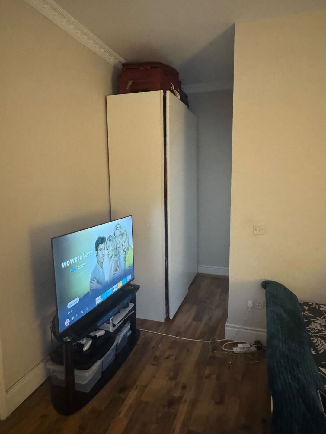 Bedroom interior with TV, wardrobe, and luggage on top. Text on screen: "We Were Liars".