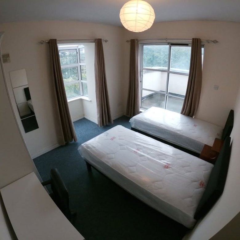 Bedroom with two beds, desk, and natural light from windows/balcony.