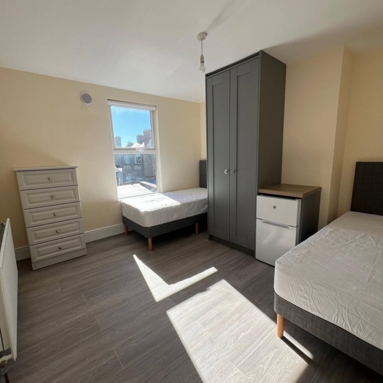 Bedroom with two beds, grey wardrobe and chest of drawers, natural light.
