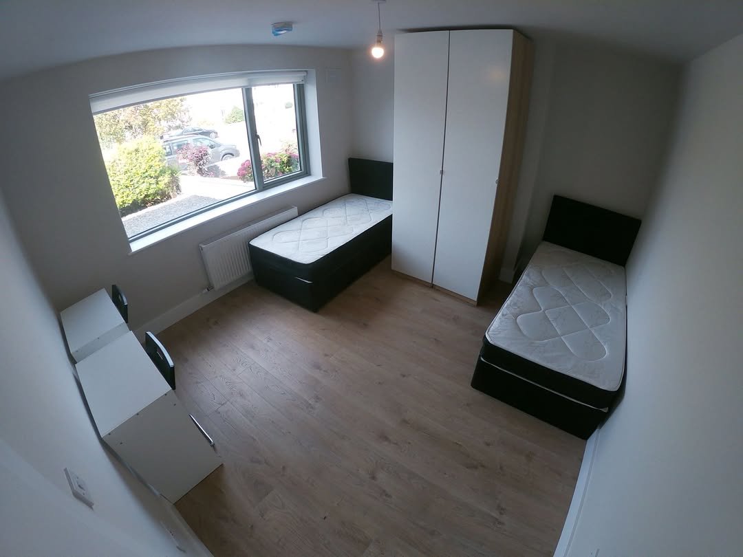 Bedroom with two beds, wardrobe, desk, and natural light from a window.