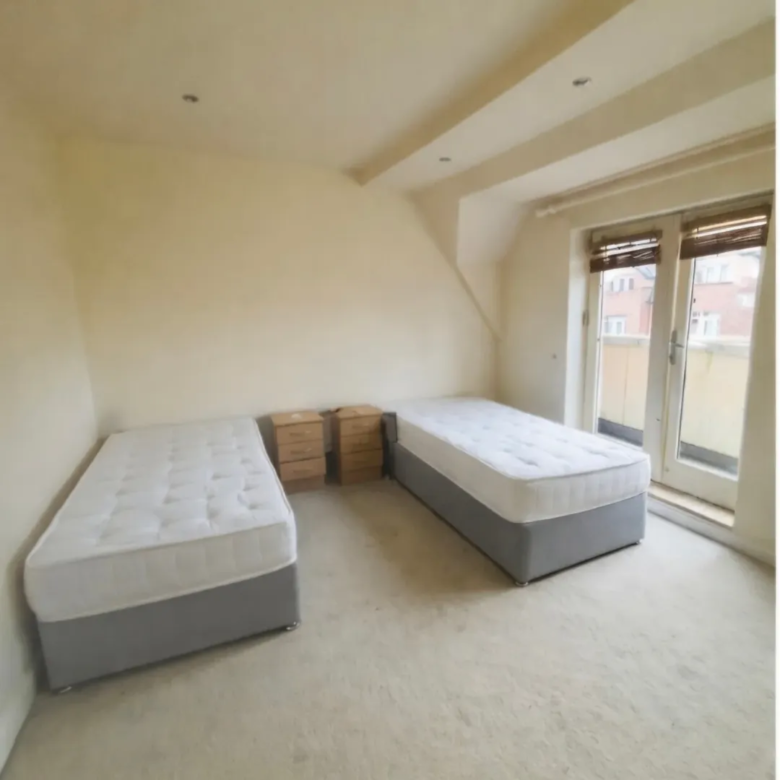 Bedroom with two single beds, nightstands, and a balcony door with blinds. Neutral color scheme.