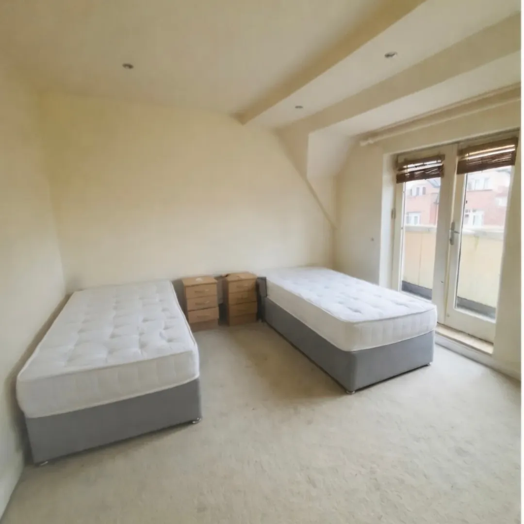 Bedroom with two single beds, nightstands, and a balcony door with blinds. Neutral color scheme.